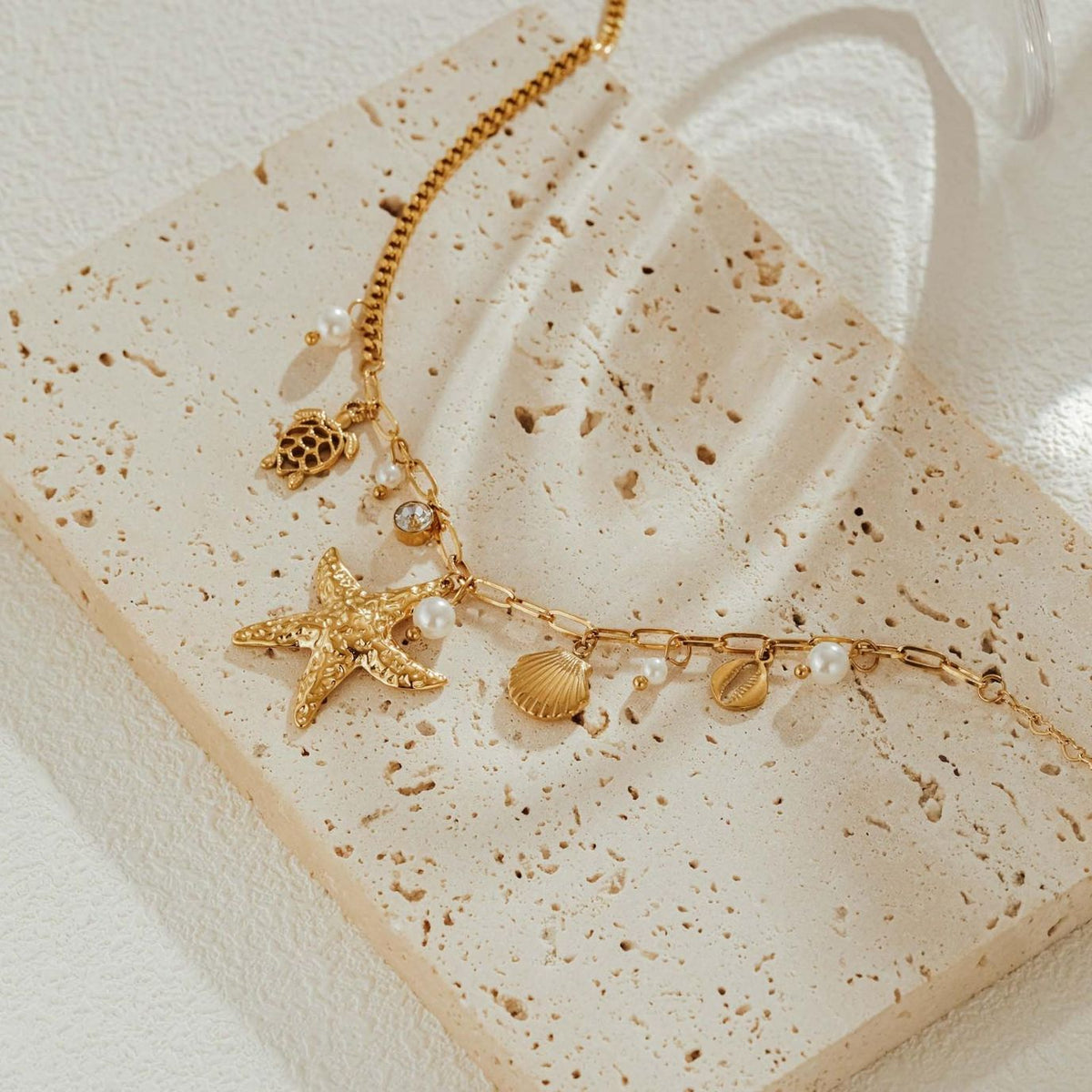 Close-up of the hammered starfish, sea turtle, cowrie and scallop shell charms and faux pearls on travertine