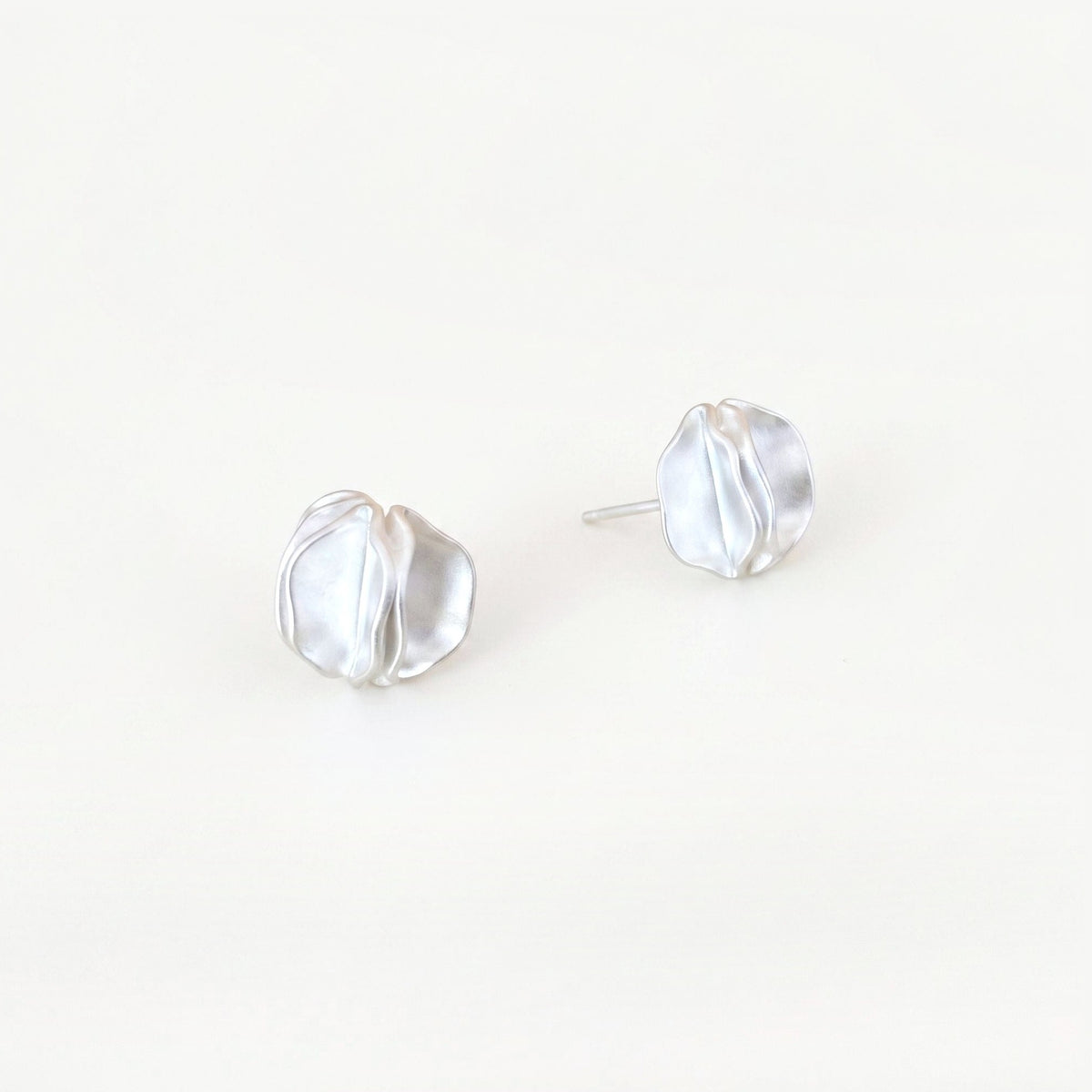Pair of sterling silver statement stud earrings with folded petal detail on a plain near-white background