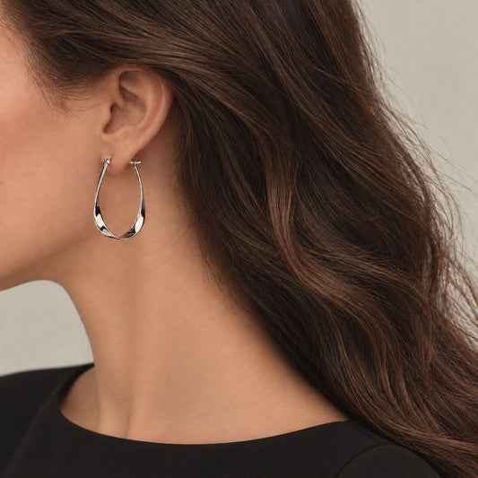 Woman wearing a sterling silver twisted teardrop hoop earring, side profile with long brown hair and a black top
