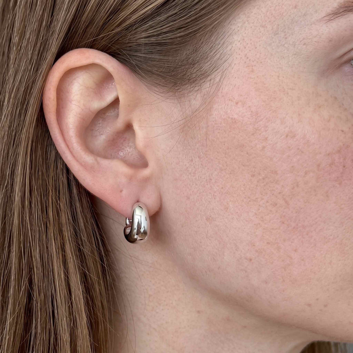 Sterling silver U hoop huggie earring worn on ear, close up showing the polished tapered dome