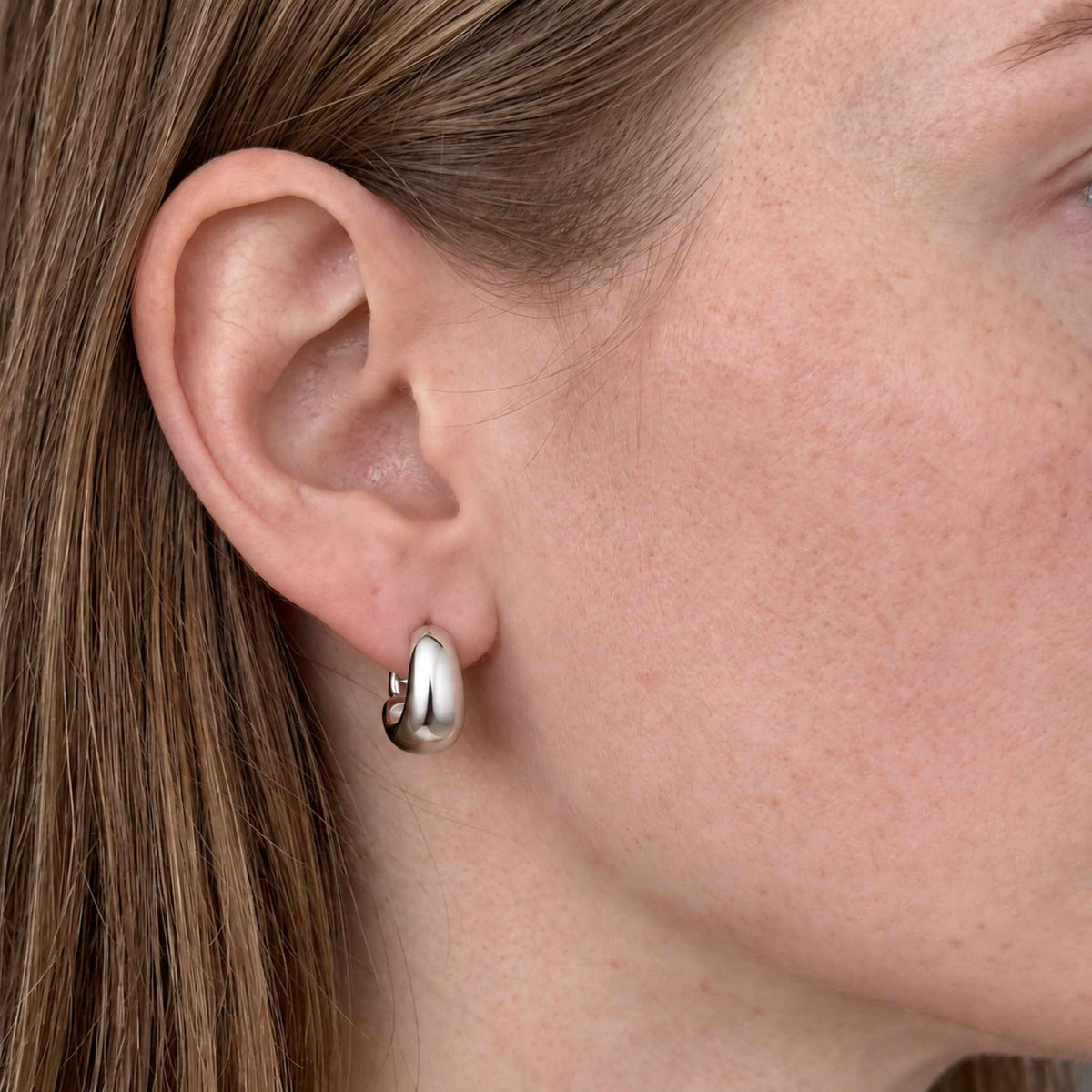 Sterling silver U hoop huggie earring worn on ear, close up showing the polished tapered dome