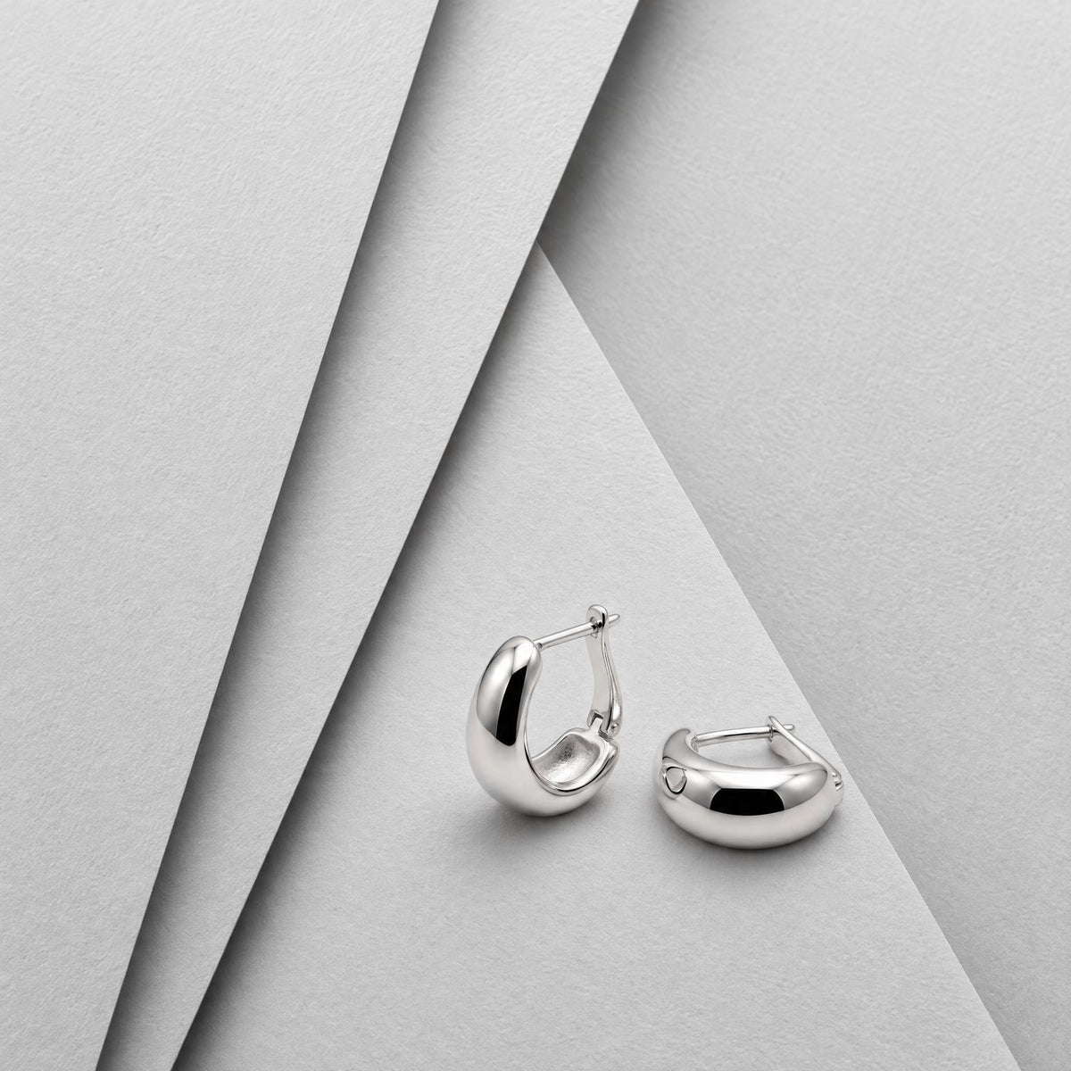 Sterling silver U hoop huggie earrings on layered grey card, one standing to show the tapered dome and hinged back