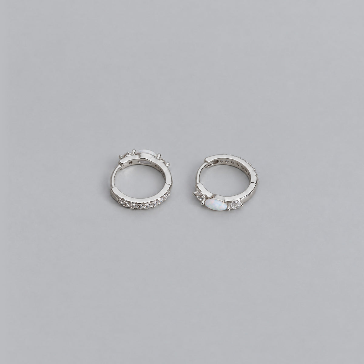 White gold opal huggie earrings lying side by side on a dove grey backdrop, cubic zirconia lined band and marquise opal