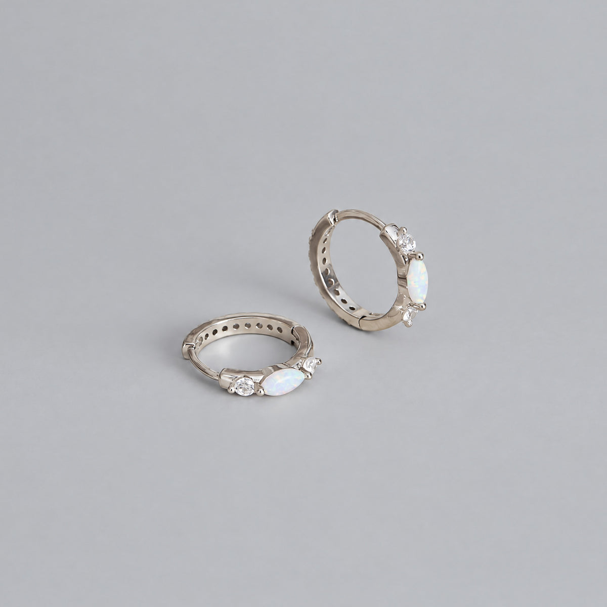 White gold opal huggie hoops on a dove grey backdrop, one standing upright and one lying flat to show the opal